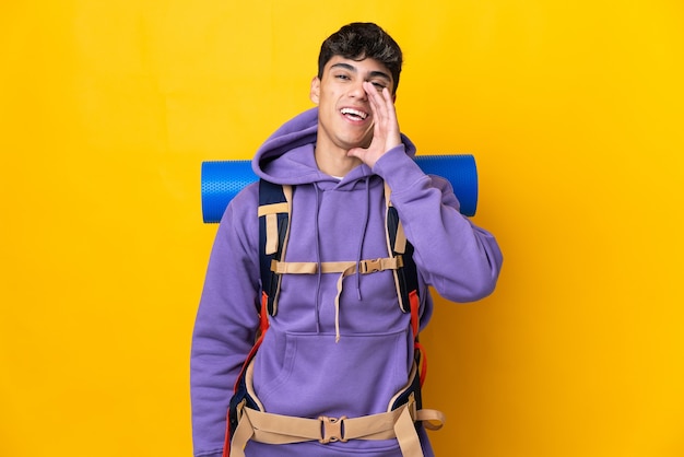 Homme jeune alpiniste avec un gros sac à dos sur mur jaune isolé criant avec la bouche grande ouverte