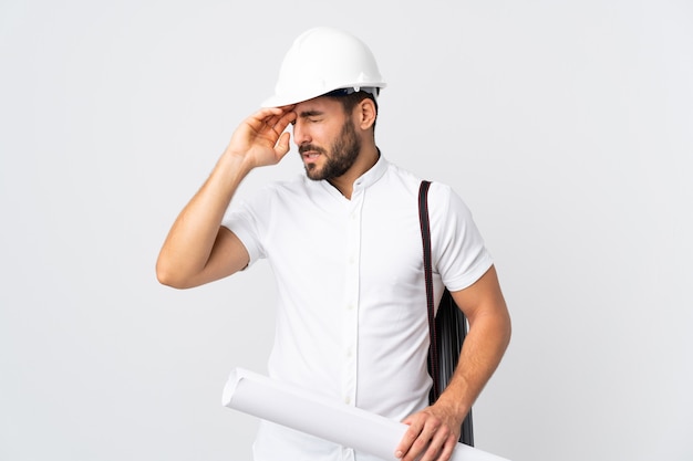 Homme jeune architecte avec casque et tenant des plans isolés sur un mur blanc avec une expression fatiguée et malade