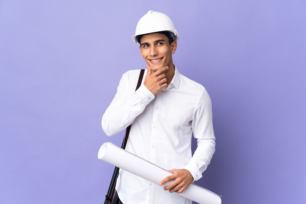 Homme jeune architecte isolé sur le mur à la recherche sur le côté et souriant