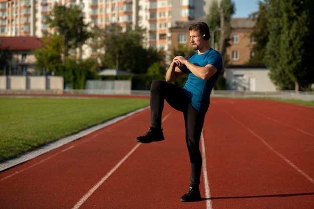 Homme jeune athlète en vêtements de sport réchauffant avant l'entraînement et écoutant de la musique dans les écouteurs. Espace libre