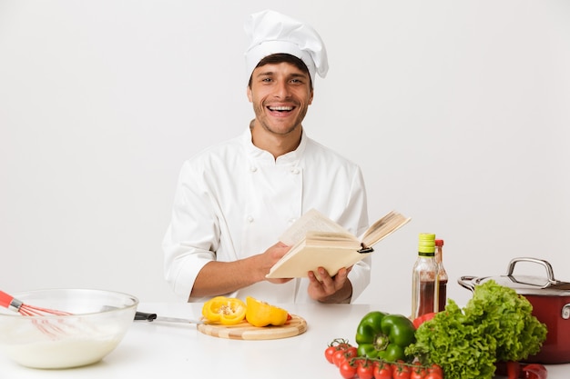 Homme jeune chef isolé sur mur blanc cuisine livre de lecture.