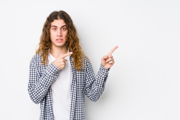 Homme jeune cheveux longs posant isolé choqué pointant avec l'index vers un espace de copie.