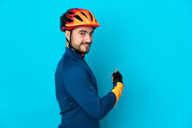 Homme jeune cycliste isolé sur mur bleu pointant vers l'arrière