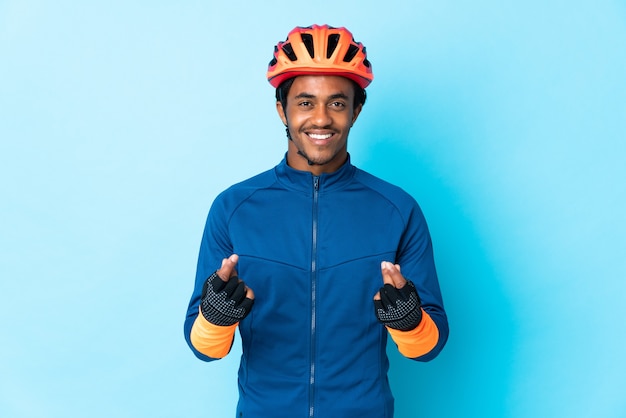 Homme jeune cycliste avec des tresses sur fond isolé faisant le geste de l'argent