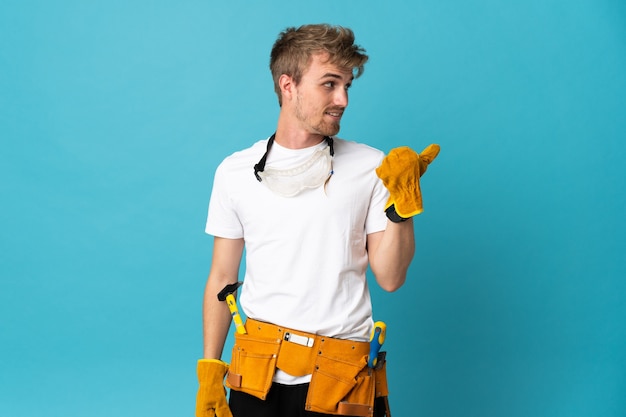 Homme jeune électricien sur mur isolé pointant vers le côté pour présenter un produit