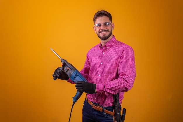 Homme jeune entrepreneur tenant une perceuse à percussion sur fond jaune avec un espace libre pour le texte. Concept de construction et de réparation