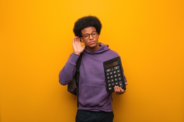 Homme jeune étudiant afro-américain tenant une calculatrice essayer d'écouter un commérage