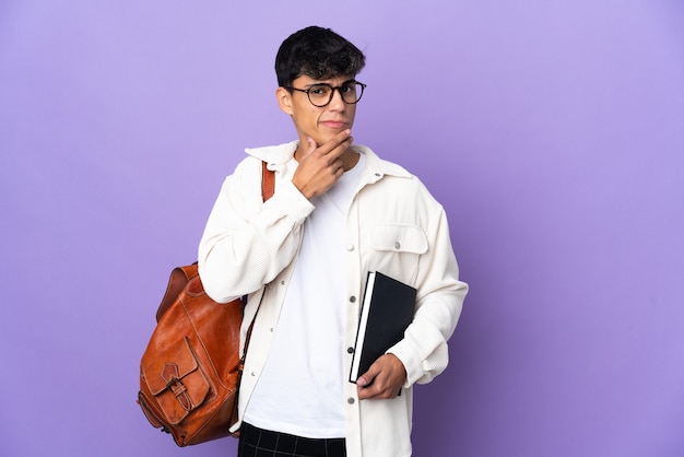 Homme jeune étudiant sur fond violet isolé en regardant en souriant