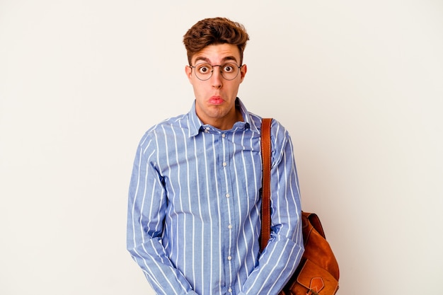 Homme jeune étudiant isolé sur fond blanc hausse les épaules et les yeux ouverts confus.