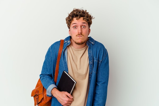 Homme jeune étudiant isolé sur fond blanc hausse les épaules et les yeux ouverts confus.