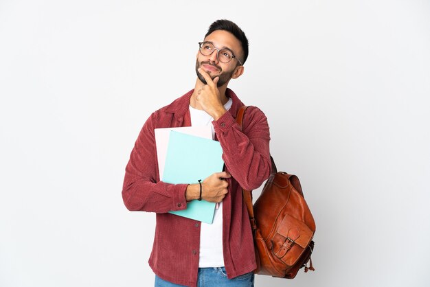 Homme jeune étudiant isolé sur un mur blanc ayant des doutes tout en levant les yeux