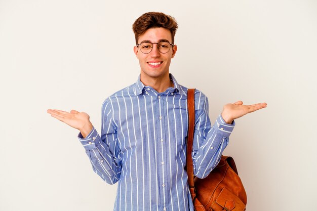 Homme jeune étudiant isolé sur un mur blanc fait échelle avec les bras, se sent heureux et confiant