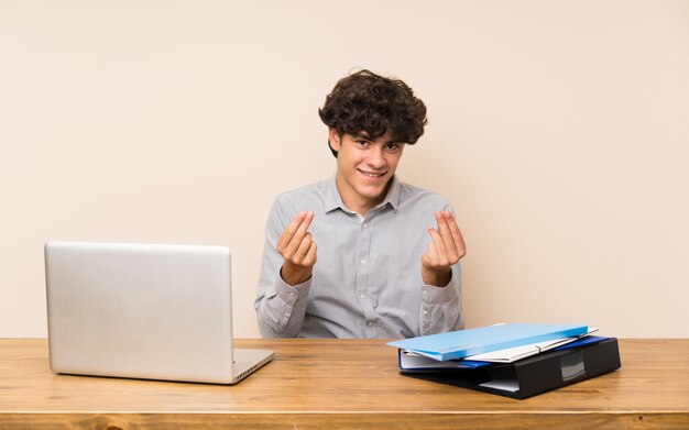 Homme jeune étudiant avec un ordinateur portable, geste d'argent