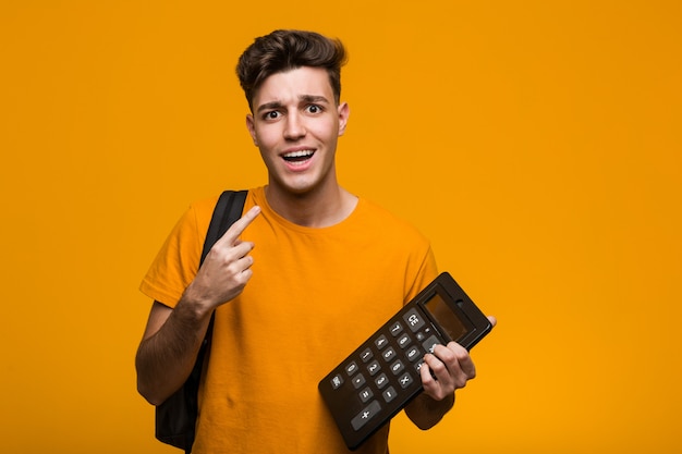 Homme jeune étudiant tenant une calculatrice montrant le poing, expression faciale agressive.