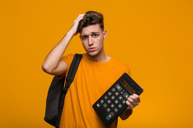 Homme jeune étudiant tenant une calculatrice sourires joyeux pointant vers l'avant.