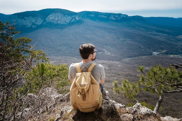 Homme jeune hipster dans les montagnes du printemps. Hipster avec un sac à dos dans le dos part en voyage