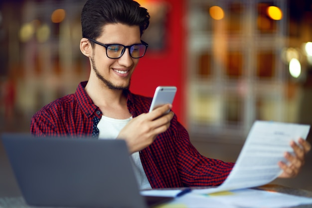 Homme jeune hipster souriant dans des verres avec ordinateur portable sur la table. Programmeur, développeur web, designer travaillant au bureau.