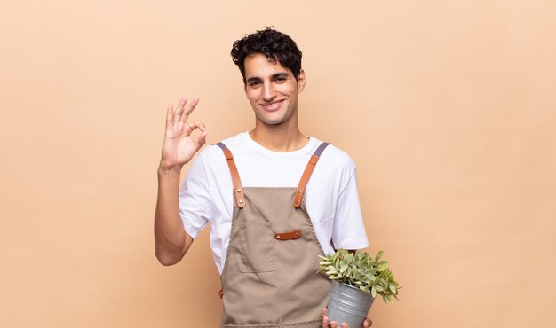 Homme jeune jardinier se sentir heureux, détendu et satisfait, montrant son approbation avec un geste correct, souriant