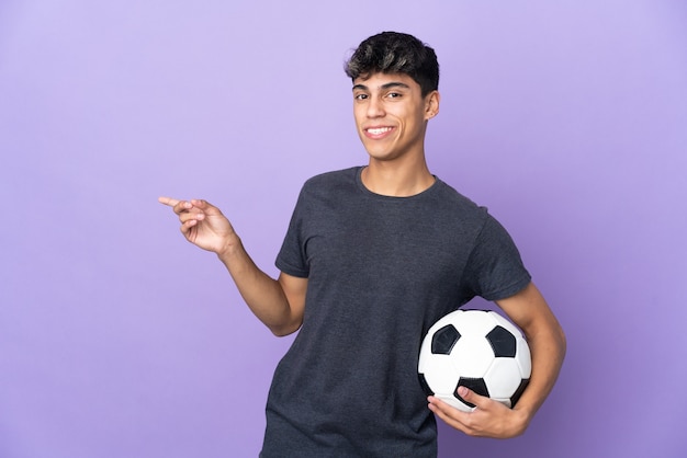 Homme jeune joueur de football sur fond violet isolé pointant le doigt sur le côté