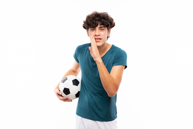 Homme jeune joueur de football sur mur blanc isolé, chuchotant quelque chose
