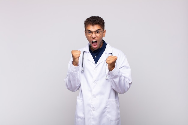 Homme jeune médecin criant de manière agressive avec une expression de colère ou les poings serrés célébrant le succès