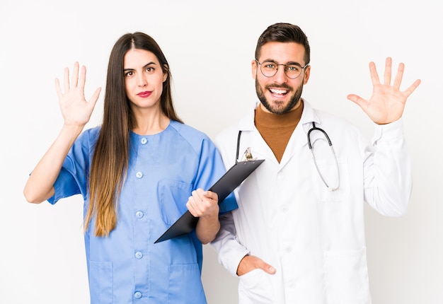 Homme jeune médecin et une infirmière isolée souriant joyeux montrant le numéro cinq avec les doigts.