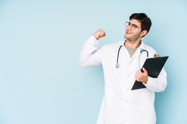 Homme jeune médecin isolé sur fond bleu levant le poing après une victoire, concept gagnant.