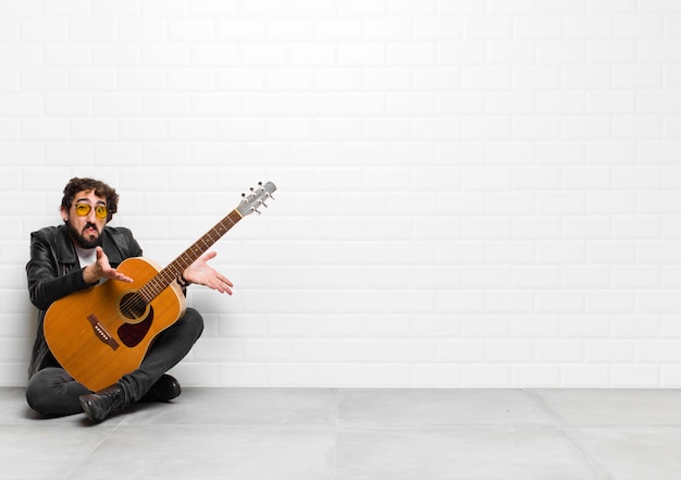 Homme jeune musicien se sentant désemparé et confus, n'ayant aucune idée, absolument perplexe avec un regard stupide ou stupide avec un concept de guitare, de rock and roll