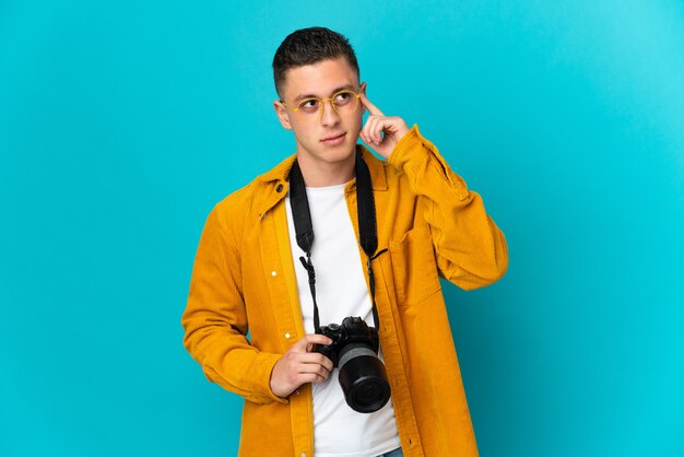 Homme jeune photographe caucasien isolé sur bleu ayant des doutes et de la pensée