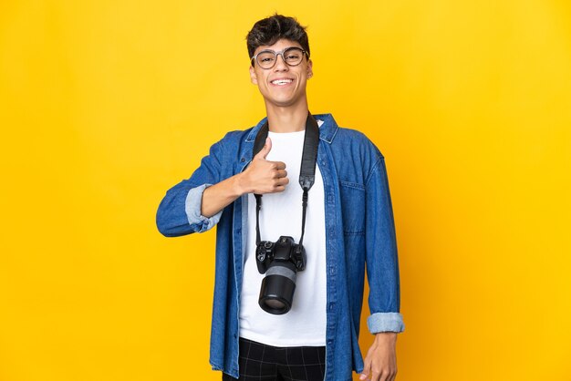 Homme jeune photographe sur fond jaune isolé donnant un geste de pouce en l'air