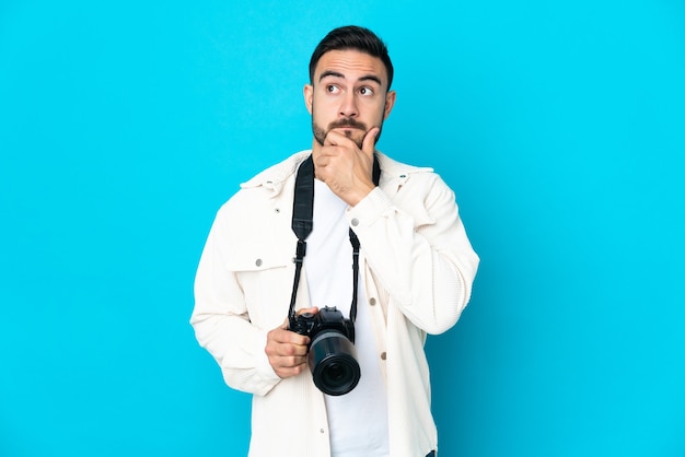 Homme jeune photographe isolé sur fond bleu ayant des doutes et de la pensée