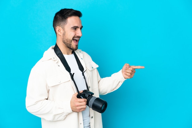 Homme jeune photographe isolé sur fond bleu pointant le doigt sur le côté et présentant un produit