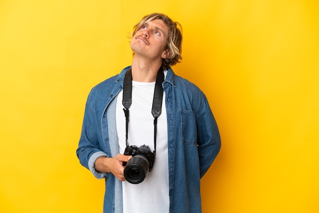 Homme jeune photographe isolé sur fond jaune et levant les yeux