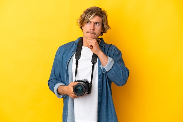 Homme jeune photographe isolé sur mur jaune ayant des doutes et de la pensée