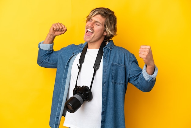 Homme jeune photographe isolé sur mur jaune célébrant une victoire