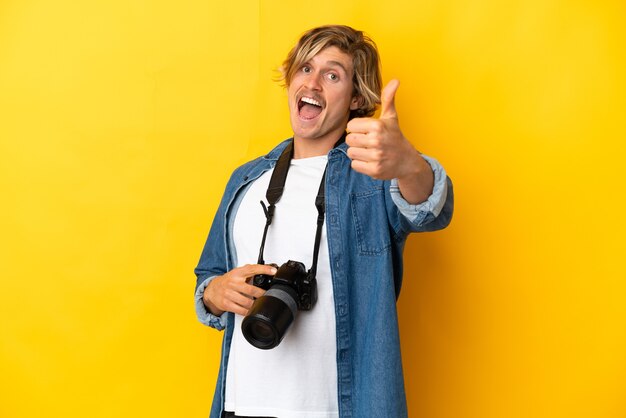 Homme jeune photographe isolé sur mur jaune avec les pouces vers le haut parce que quelque chose de bien s'est passé