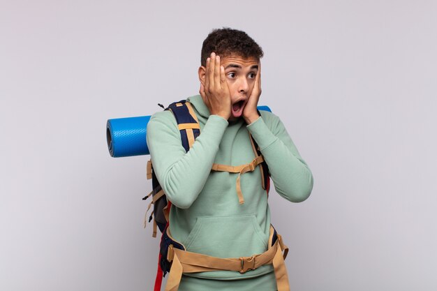 Homme jeune randonneur se sentir heureux, excité et surpris, regardant sur le côté avec les deux mains sur le visage