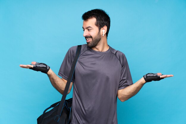 Homme jeune sport avec barbe sur bleu isolé tenant copyspace avec deux mains