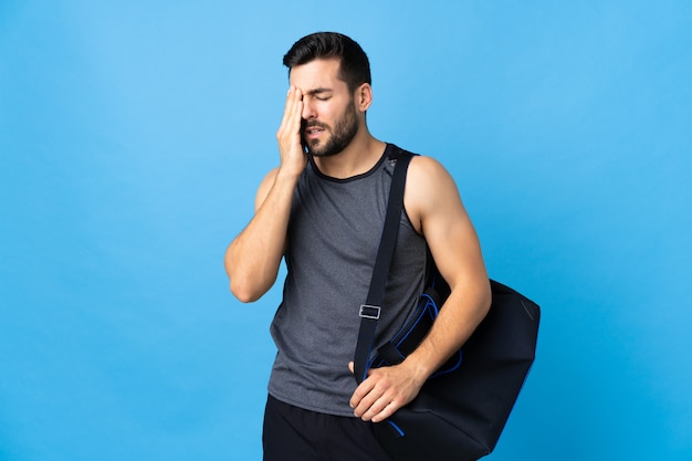 Homme jeune sport avec sac de sport isolé sur mur bleu avec maux de tête
