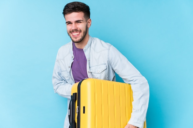 Homme jeune voyageur caucasien tenant une valise isolée rire et s'amuser.