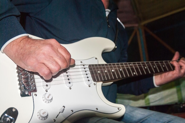 Un homme joue d'une guitare électrique blanche.