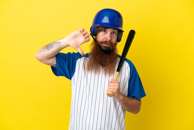 Homme de joueur de baseball rousse avec casque et batte isolé sur fond jaune montrant le pouce vers le bas avec une expression négative