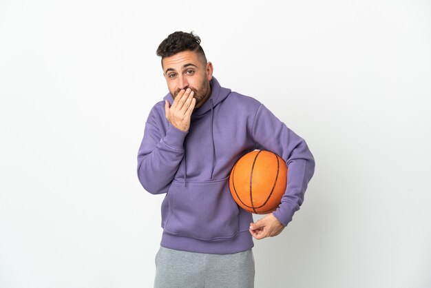 Homme de joueur de basket-ball isolé sur blanc heureux et souriant couvrant la bouche avec la main