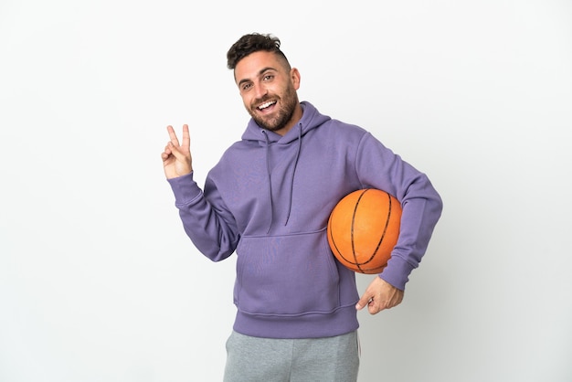 Homme de joueur de basket-ball isolé sur fond blanc souriant et montrant le signe de la victoire