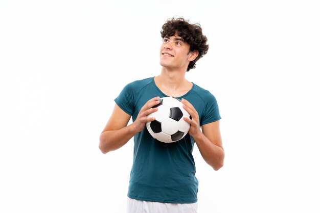 Homme de joueur de football jeunes sur mur blanc isolé, levant en souriant