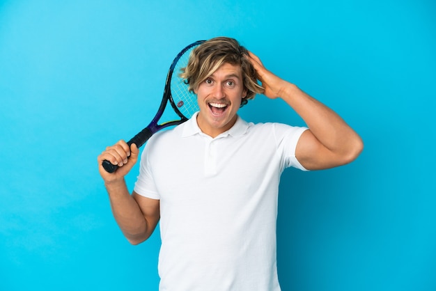 Homme de joueur de tennis blonde isolé sur bleu avec une expression de surprise