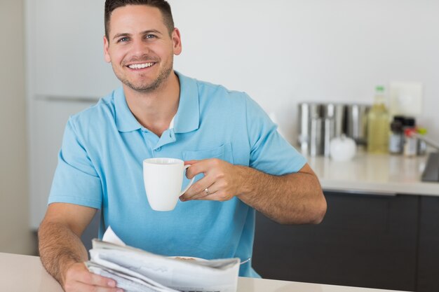 Homme avec journal tenant une tasse de café à table