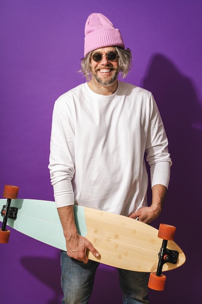 Un homme joyeux d'âge moyen avec un longboard portant un sweat-shirt blanc sur un fond violet