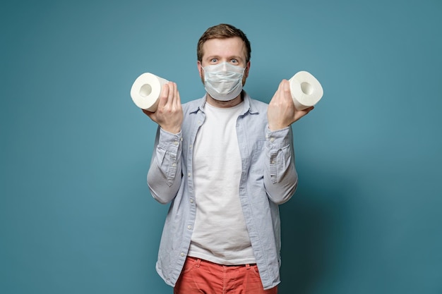 Un homme joyeux dans un masque médical tient dans les mains des rouleaux de papier toilette qu'il a réussi à acheter