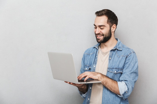 Homme joyeux excité portant chemise isolé sur mur gris, montrant un ordinateur portable